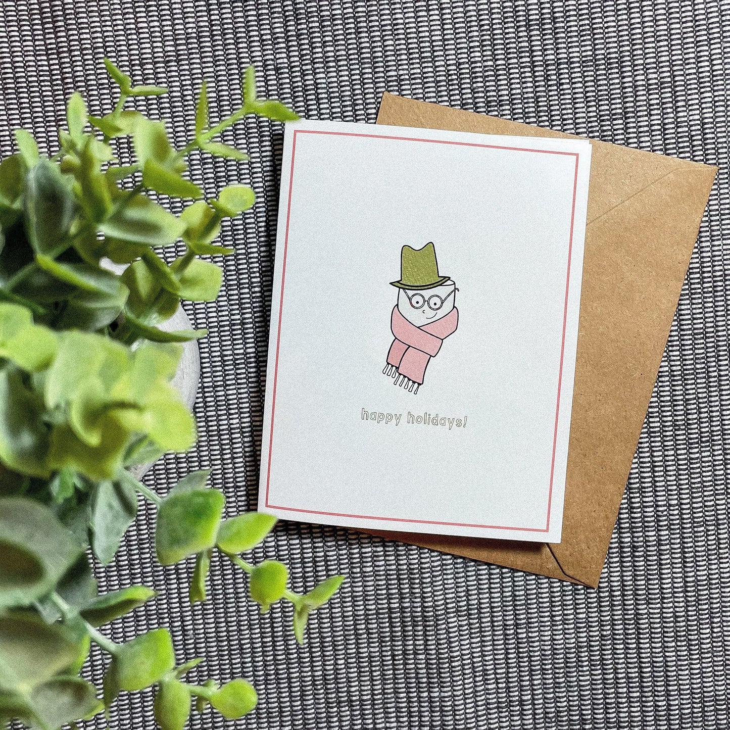 This holiday card features a drawing of a cute little marshmallow man with a scarf and a top hat with the text 'happy holidays!"