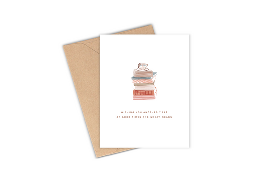 This greeting card features a drawing of a stack of books with a mug of tea sitting on top with the phrase "wishing you another year of good times and great reads" with a vintage, retro looking vibe